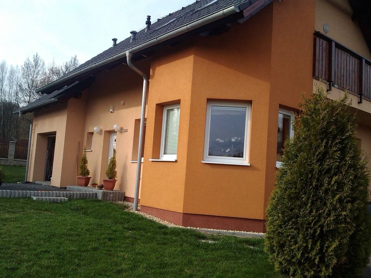 Rodinný dům s oranžovou strukturovanou fasádou a bílými plastovými okny – realizace