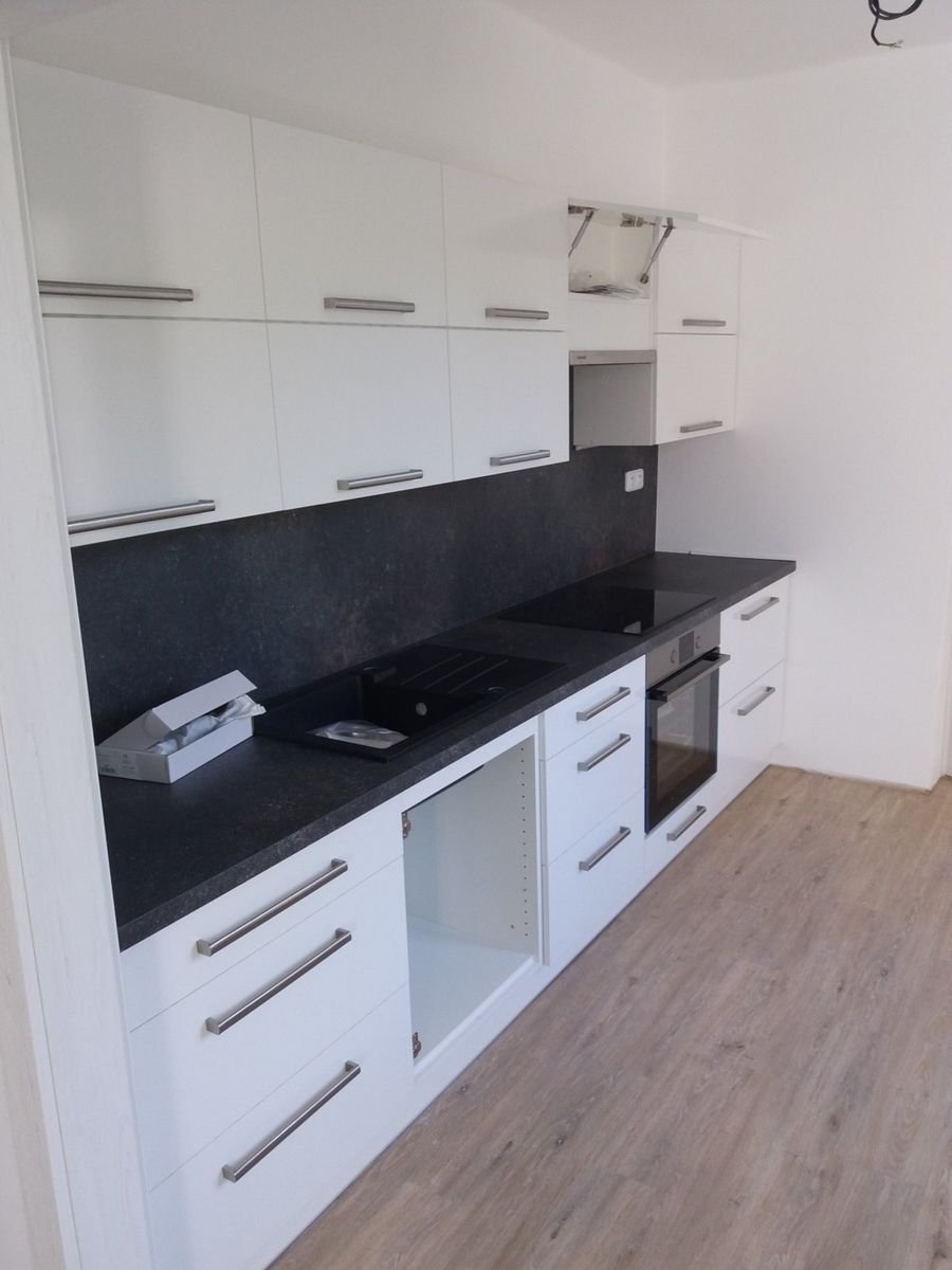 Bílá kuchyňská linka s tmavou pracovní deskou a zástěnou – realizace